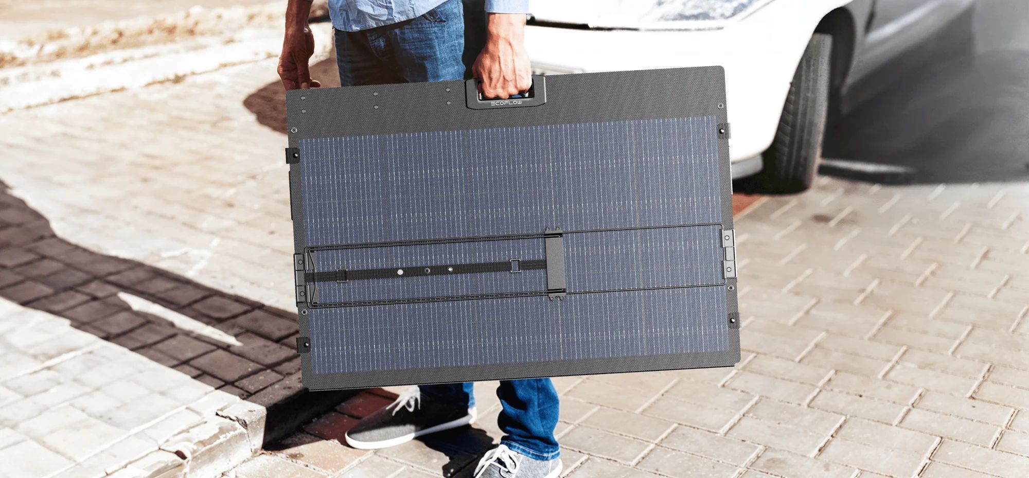 אדם נושא פאנל EcoFlow 400W NextGen במצב מקופל באמצעות הידית לצד רכב